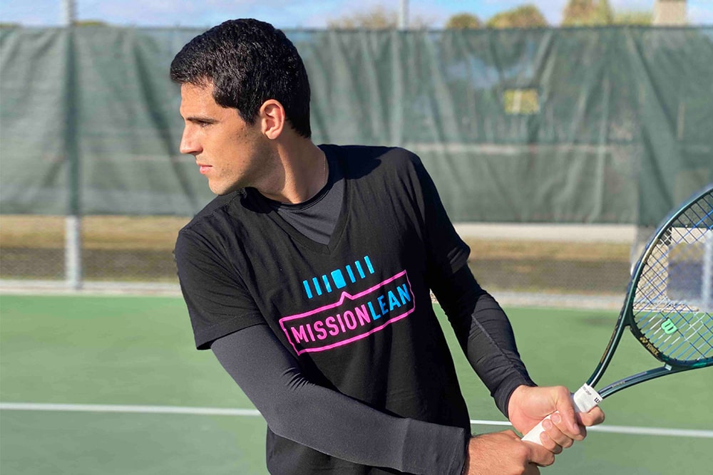Tennis Player Wears Mission Lean T-Shirt and Holds Racquet on the Tennis Court.